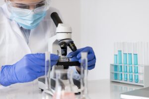 Pathologist examining a microscope slide with test tubes in the background.