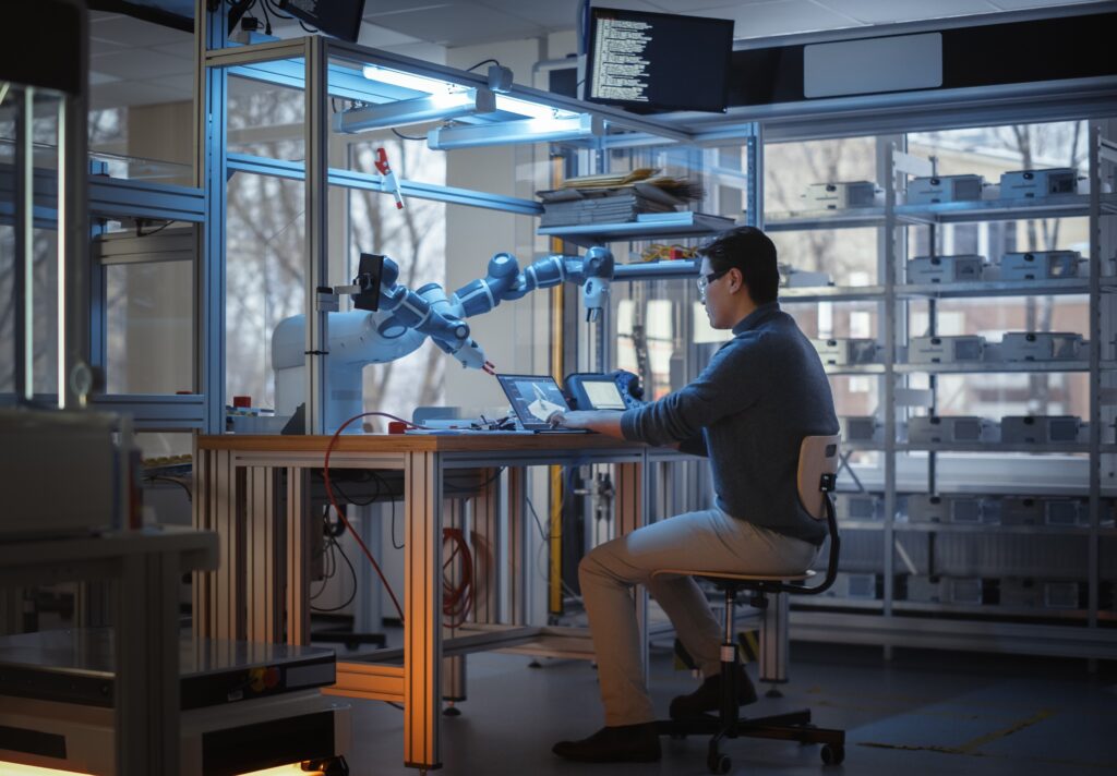 Scientist overseeing a robotic laboratory system performing automated experiments at a computer workstation.